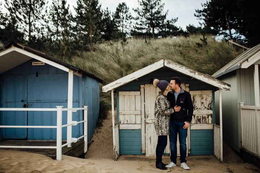 cuddling couple standing in front of a beach hut on a beach 