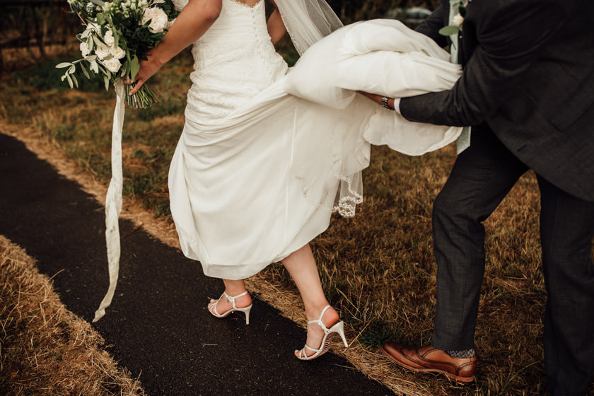 groom holding brides train showing off her shoes and walking photographed by Wedding Photography Northampton